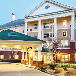 The image shows a well-lit hotel entrance with prominent columns and manicured landscaping.