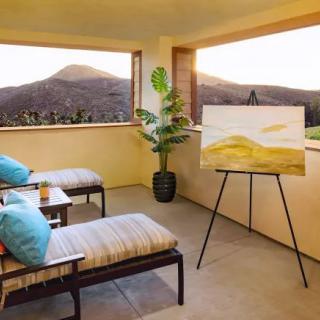 A peaceful balcony setup with reclining chairs, a scenic mountain view, and an art easel displaying a painting.