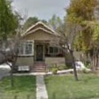 A quaint residential house with a front porch, surrounded by trees and a green lawn.