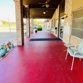 A covered outdoor patio with a bright red floor, chairs, and potted plants.