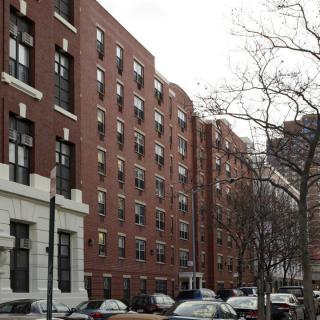 A row of urban apartment buildings with cars parked along the street.