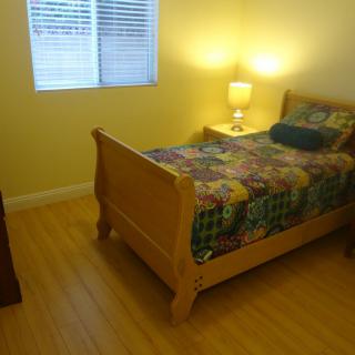 A cozy bedroom with a single bed, nightstand, and lamp by the window.