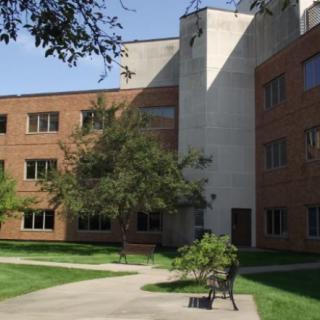 A view of a multi-story building with trees and a bench outside.