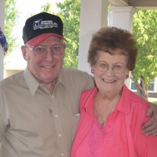 An elderly couple smiling while posing together outdoors.