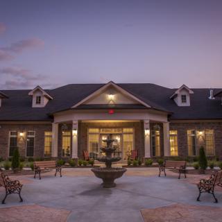 A beautifully lit building at dusk with a central fountain and surrounding benches.