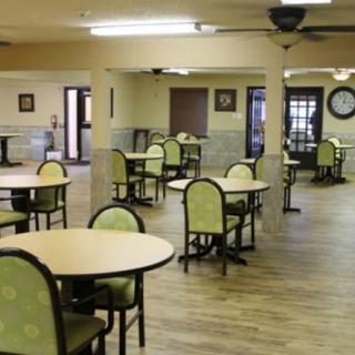 An empty dining area with round tables and green chairs on a wooden floor.