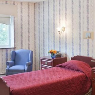 A cozy bedroom with a red bedspread, striped wallpaper, and a blue armchair by the window.
