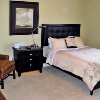 A cozy bedroom with a bed, nightstand, lamp, and chair.