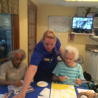 Caregiver assisting elderly individuals with a painting activity at a community center.