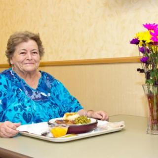 A woman sits at a table in a restaurant with a tray of food and a vase of flowers.