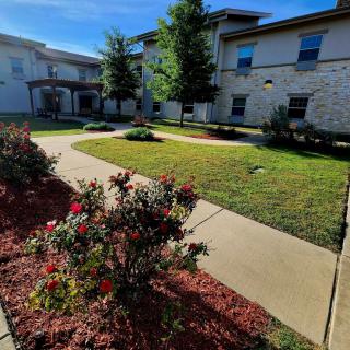 A landscaped courtyard featuring a pathway, flowers, and trees in front of a building.