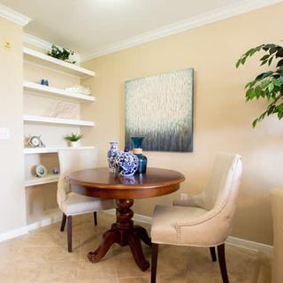 A cozy dining area with a round wooden table, upholstered chairs, and decorative elements on shelves.