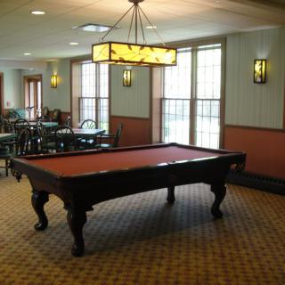 A pool table in a well-lit recreation room with carpet flooring and dining tables.
