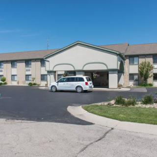 A hotel building with a parking lot and a white vehicle parked in front during the daytime.