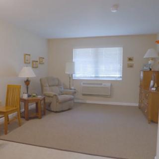 A cozy living room with simple furnishings, including a chair, table, and lamps.