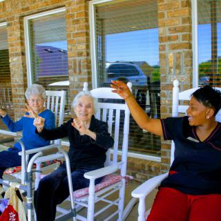 Seniors exercising outdoors with a caregiver in rocking chairs.