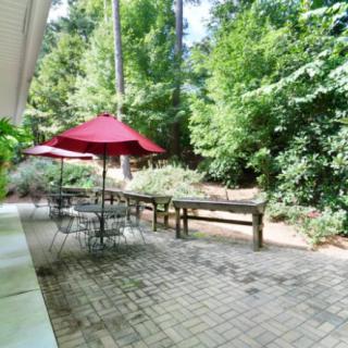 A tranquil patio area with tables and red umbrellas surrounded by lush greenery.