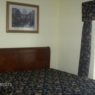 A bedroom with a neatly made bed, floral curtains, and a painting on the wall.