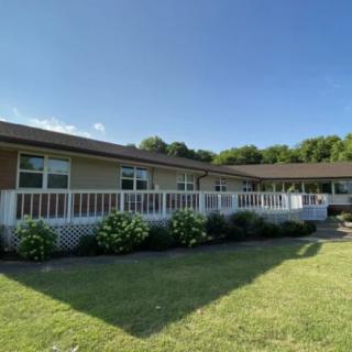A single-story house with a spacious deck and a well-maintained yard under a clear blue sky.