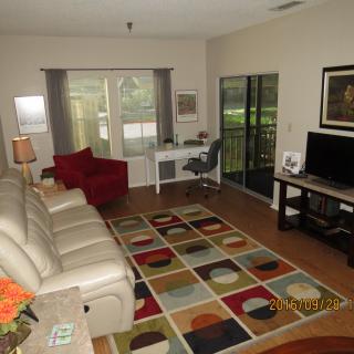 A cozy living room with a colorful rug, leather sofa, and a work desk by the window.