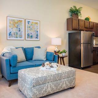 A cozy living room with a blue sofa, patterned ottoman, and decorative elements next to an open kitchen area.
