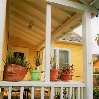 A charming front porch of a yellow house adorned with potted plants under a sunny sky.