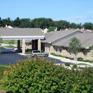 A view of a building with a parking lot and landscaping, featuring trees and bushes.