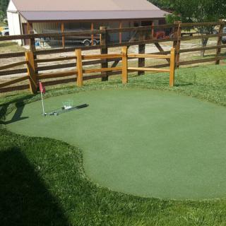 A small outdoor putting green with artificial turf, surrounded by a wooden fence.