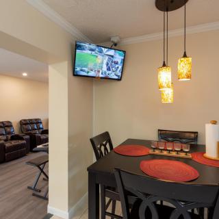 A cozy dining area with a wall-mounted TV and pendant lighting, featuring a table set with red placemats.