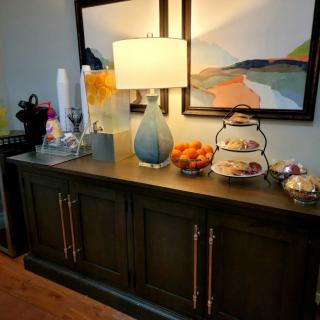 A stylish sideboard setup featuring a lamp, artwork, fruit bowl, and coffee station.