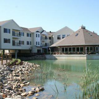 A residential building next to a tranquil pond with rocks and vegetation.