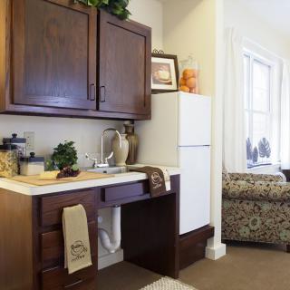 A small kitchen area with dark wood cabinets, a sink, and a white refrigerator, adorned with decorative items and towels.