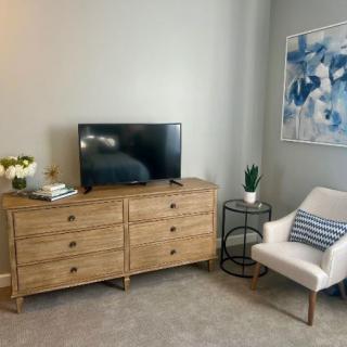 A cozy living room setup with a wooden dresser, TV, and comfortable chair, complemented by modern artwork.