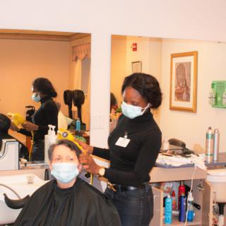 A hairstylist wearing a mask is cutting the hair of a customer, who is also masked, in a salon setting.