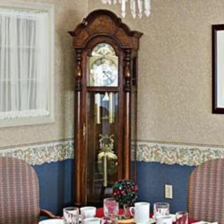 A traditional grandfather clock stands in a dining room setting, surrounded by chairs and a set dining table.