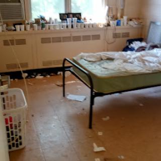 A cluttered bedroom with a mattress, a laundry basket, and scattered papers.