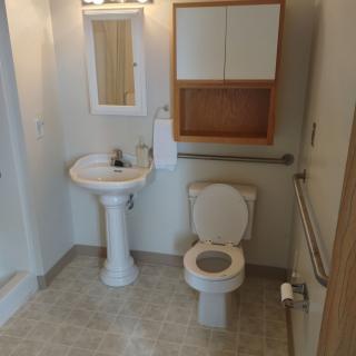A clean bathroom with a pedestal sink, toilet, wall-mounted cabinet, and safety grab bars.