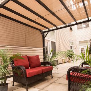 A cozy outdoor patio with a pergola, featuring comfortable seating and vibrant red cushions, surrounded by greenery.