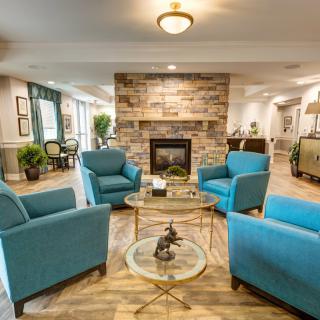A cozy and modern living room with blue armchairs arranged around a glass coffee table, centered by a stone fireplace.