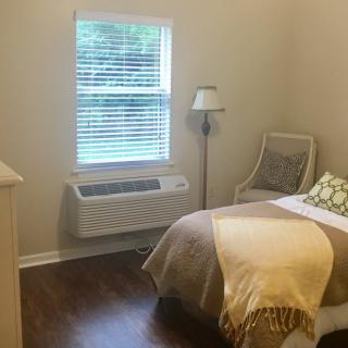A cozy bedroom with a single bed, lamp, chair, and window air conditioner.