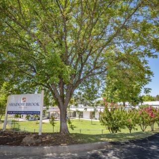 A school building surrounded by trees on a sunny day, with a sign in the foreground.