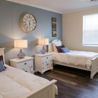 A cozy bedroom with two single beds, decorated with a large wall clock and matching nightstands with lamps.