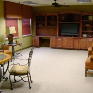 A spacious living room with wooden cabinets and a television, featuring several chairs and a table.