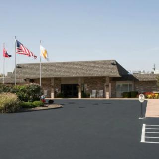 An exterior view of a building with several flags flying and a parking lot in front.