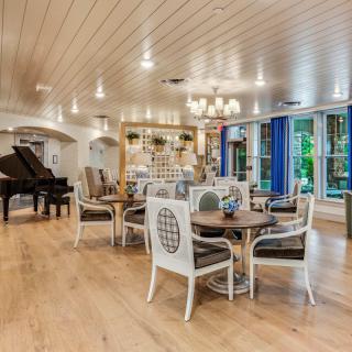 Elegant dining area with a piano and chandelier, featuring wood flooring and bright lighting.
