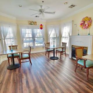 A cozy indoor dining area with several tables and chairs, illuminated by natural light from large windows.