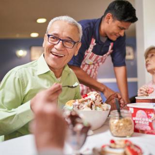 A group of people enjoying ice cream at a restaurant, with one man in focus smiling while holding a spoon.