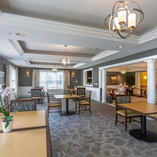 A well-lit dining area with tables and chairs, featuring chandeliers and decorative plants.