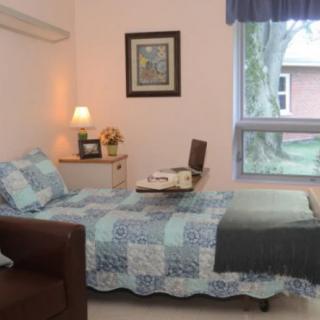A cozy bedroom with a neatly made bed, lamp, and window view.