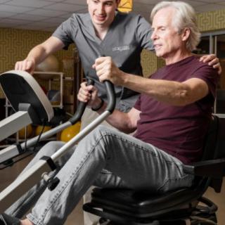 A senior man receiving assistance during a physical therapy session on an exercise machine.